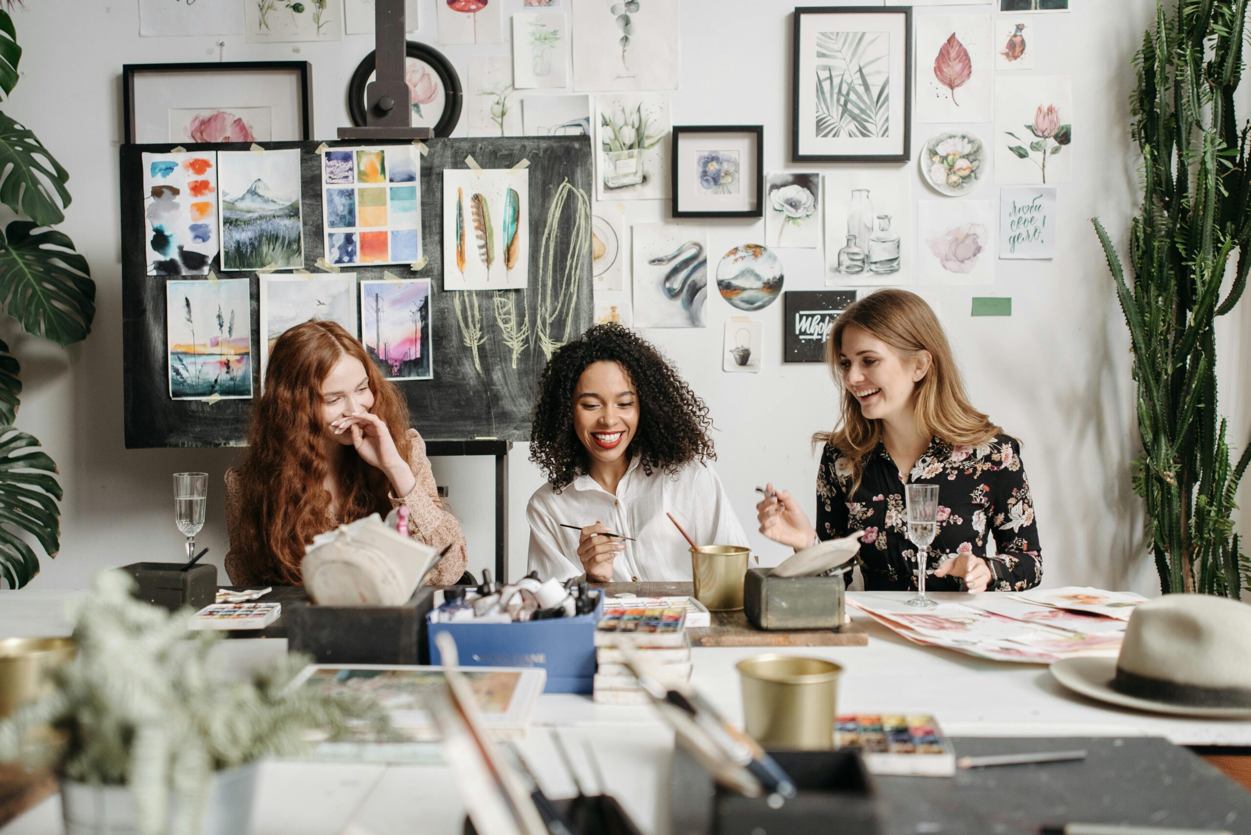 Three women enjoying a painting workshop together surrounded by art supplies and watercolor artwork.